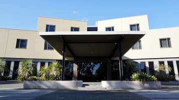 Un edificio moderno con entrada cubierta, ventanas amplias y zonas ajardinadas con plantas.