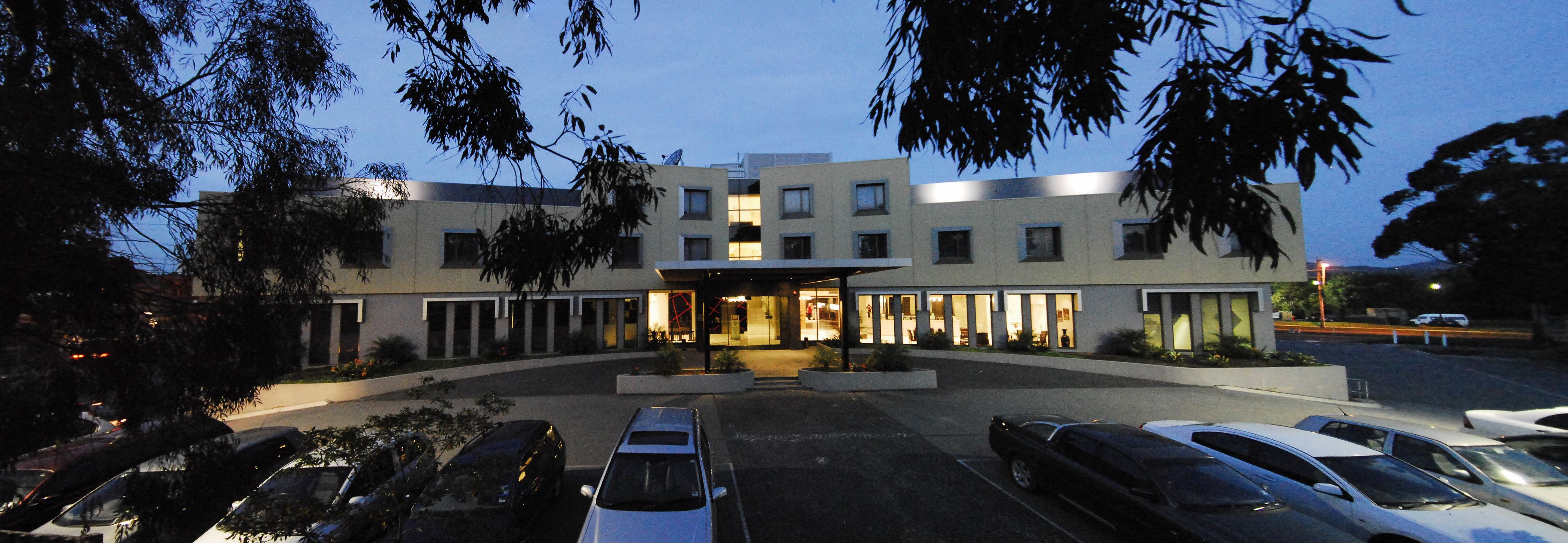 Un hôtel moderne doté d’une entrée centrale, de nombreux espaces de stationnement et d’un espace paysager agrémenté d’arbres.