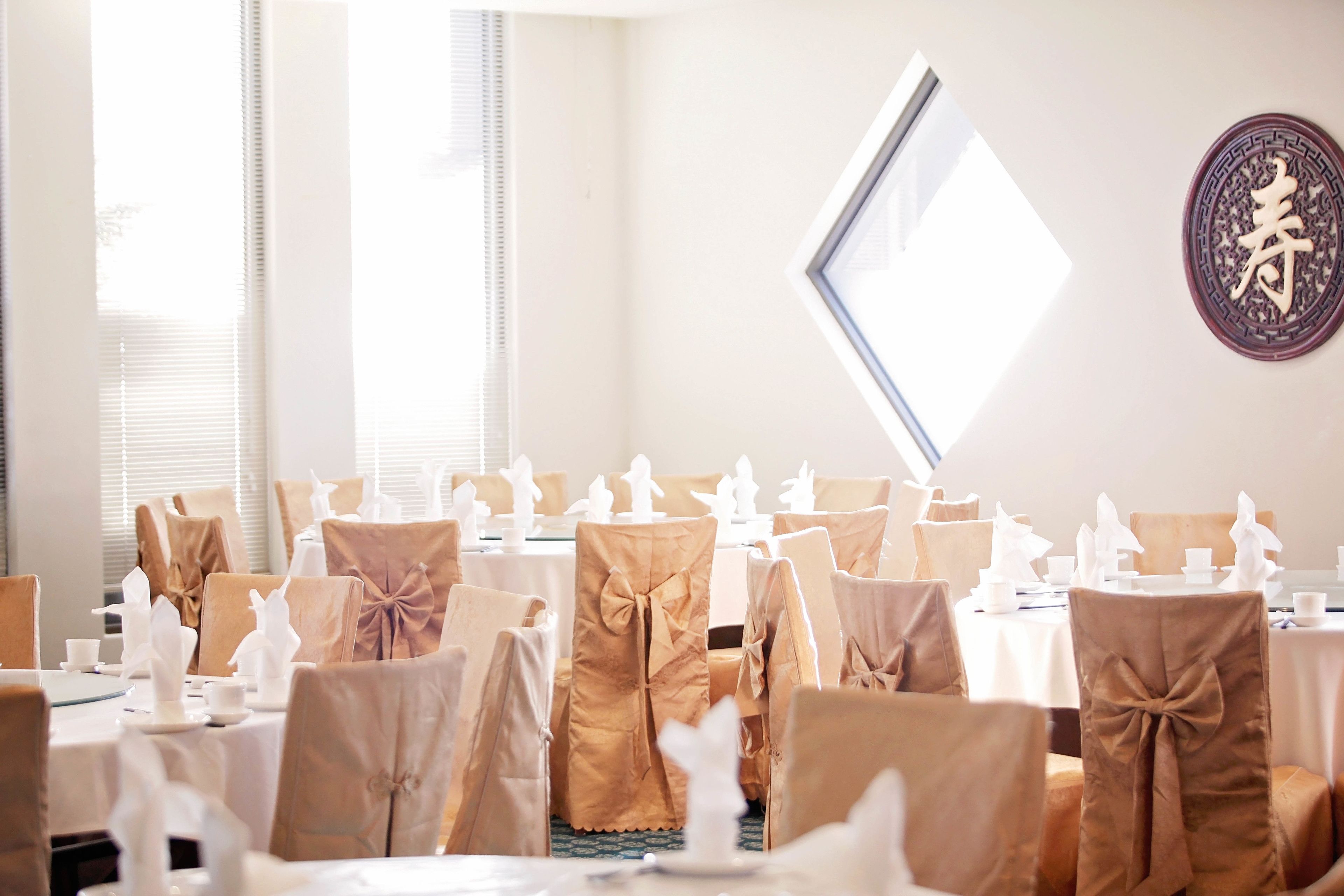 A banquet hall with tables set for a formal event, featuring brown chair covers and white table settings.
