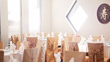Salão de banquetes com mesas montadas para um evento formal, com capas marrons nas cadeiras e louças brancas.