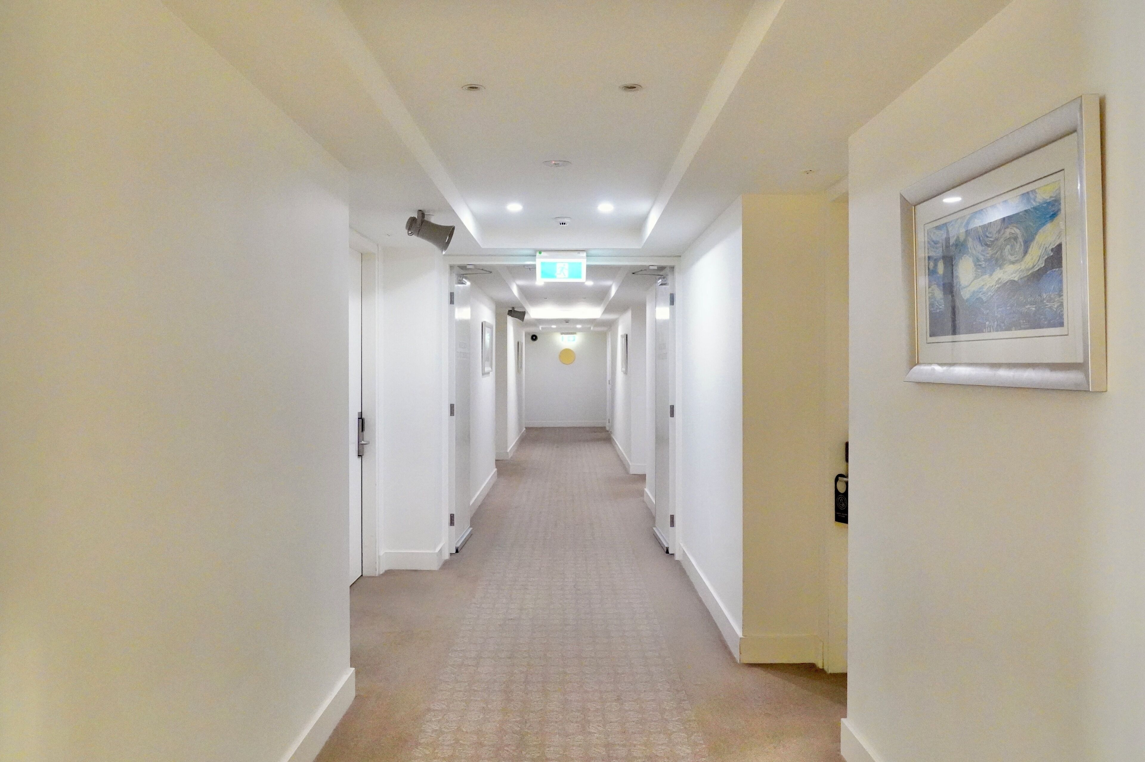 Ein Hotelgang mit weißen Wänden, einem gemusterten Teppich und einem Bild in einem Rahmen an der rechten Wand.