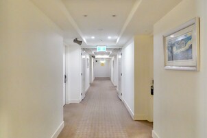 A hotel hallway with white walls, a patterned carpet, and a framed painting on the right wall.