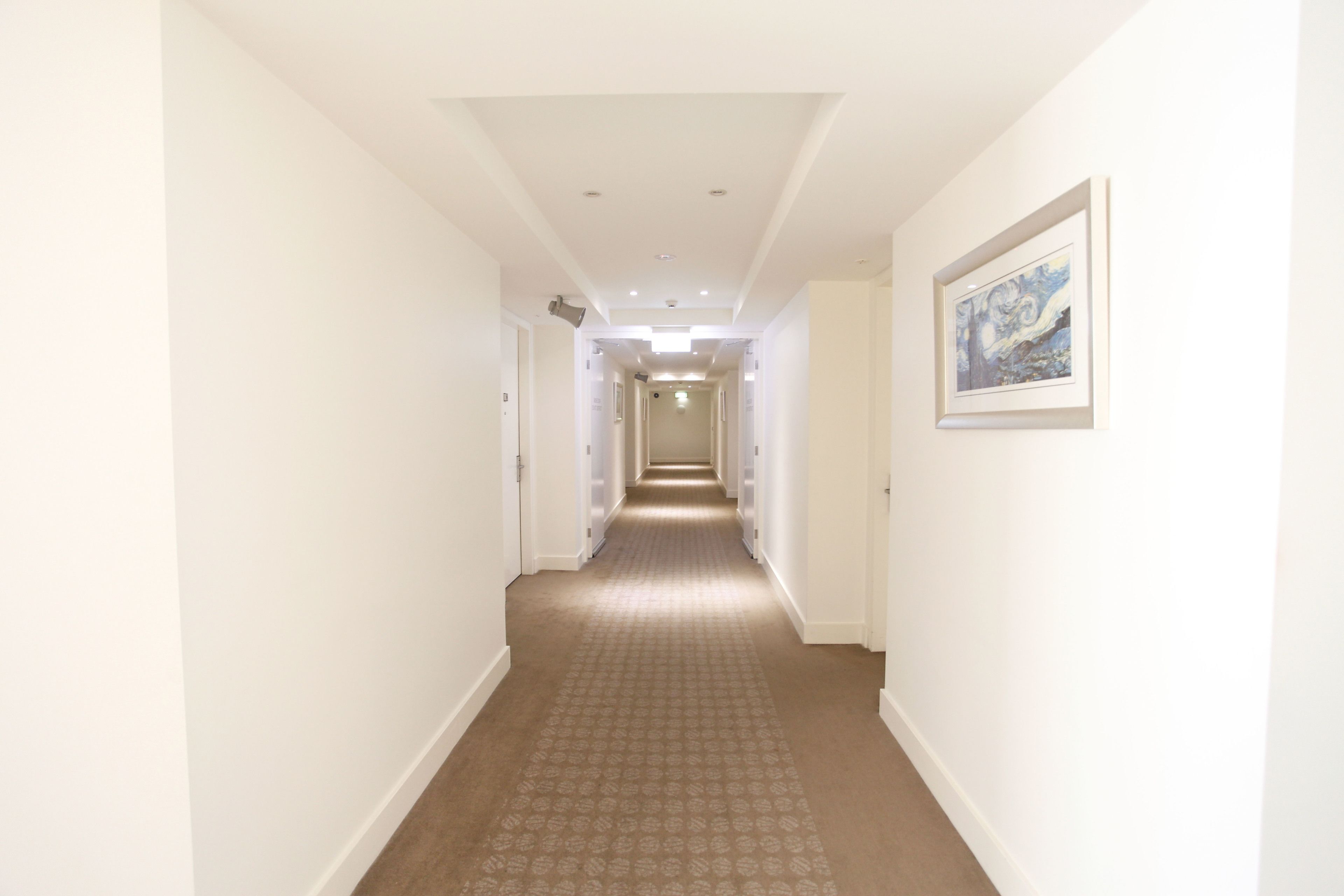 A long, narrow hallway with white walls and a patterned carpet.