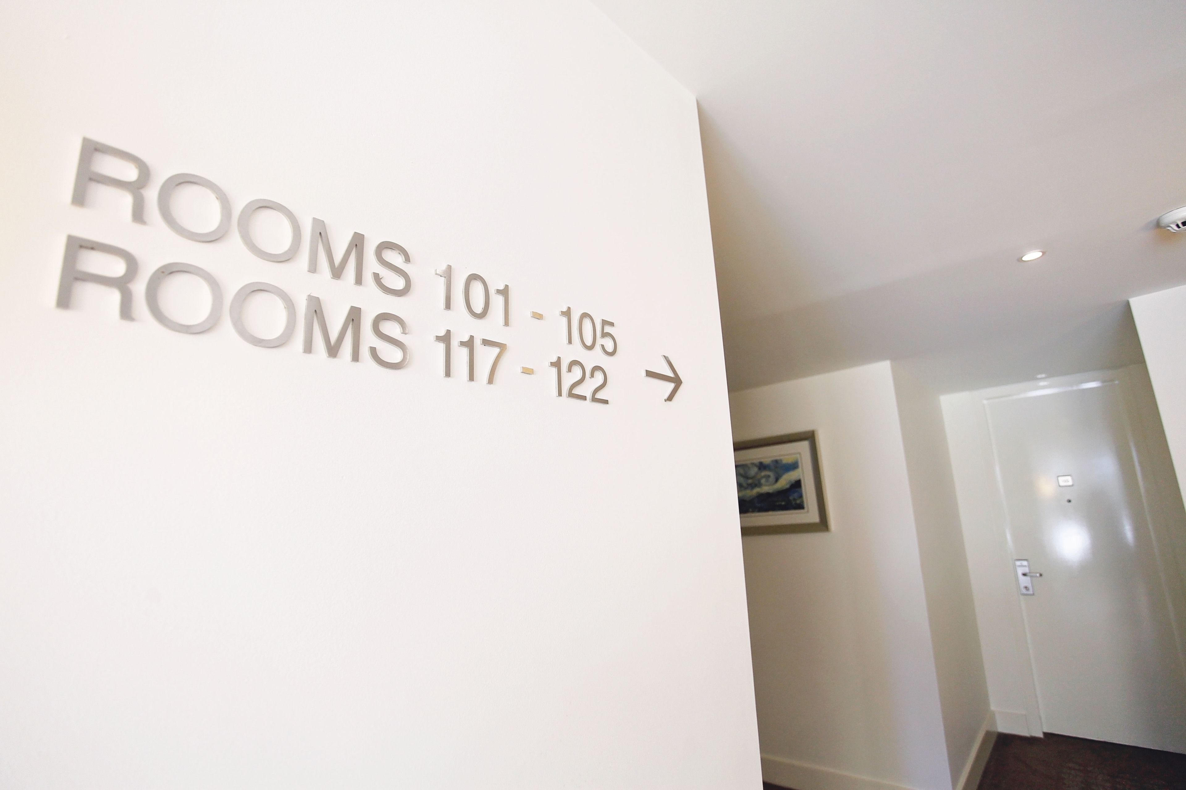 Pared con números de habitación y flechas direccionales que indican la ubicación de las habitaciones 101 a 105 y 117 a 122.