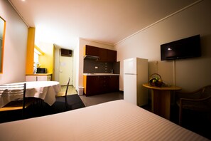 A hotel room with a bed, a dining table, a kitchen area, and a TV mounted on the wall.