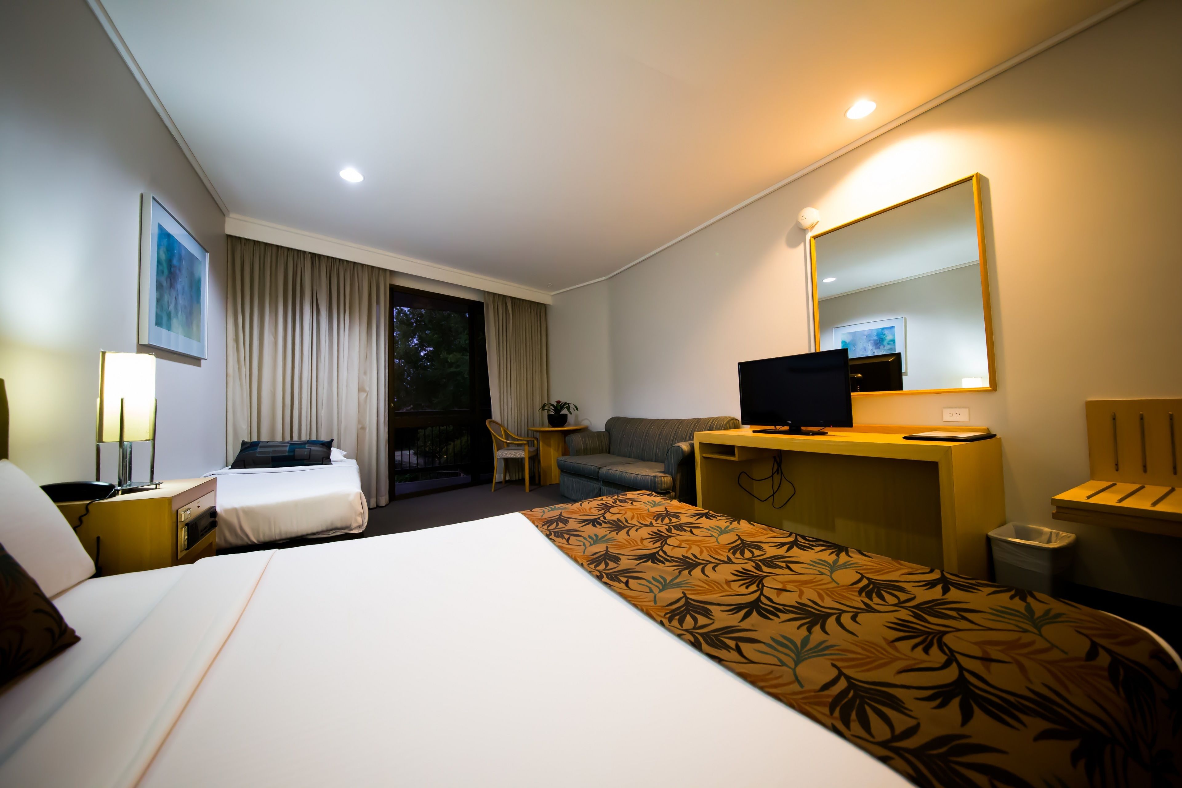A hotel room with a large bed, a desk with a computer, a sofa, a chair, and a TV.