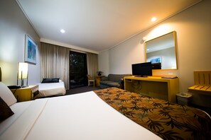 A hotel room with a large bed, a desk with a computer, a sofa, a chair, and a TV. - Sandown Regency (Noble Park)