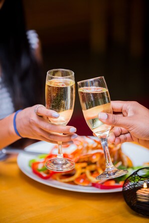 Two hands holding champagne glasses, a plate of food, and a candle on a table.
