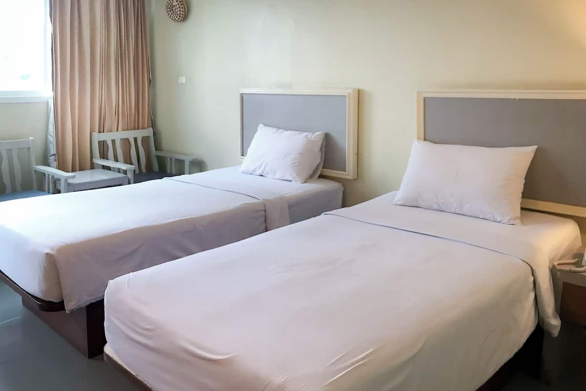 Two single beds with white linens, a small table, a chair, and a wall-mounted decorative item.