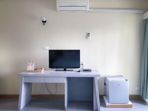 Een kamer met een wit bureau, een flatscreen-televisie, een kleine koelkast en een wandairconditioner.