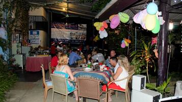 Un área de comedor al aire libre con mesas y sillas, un banderín y globos colgantes.