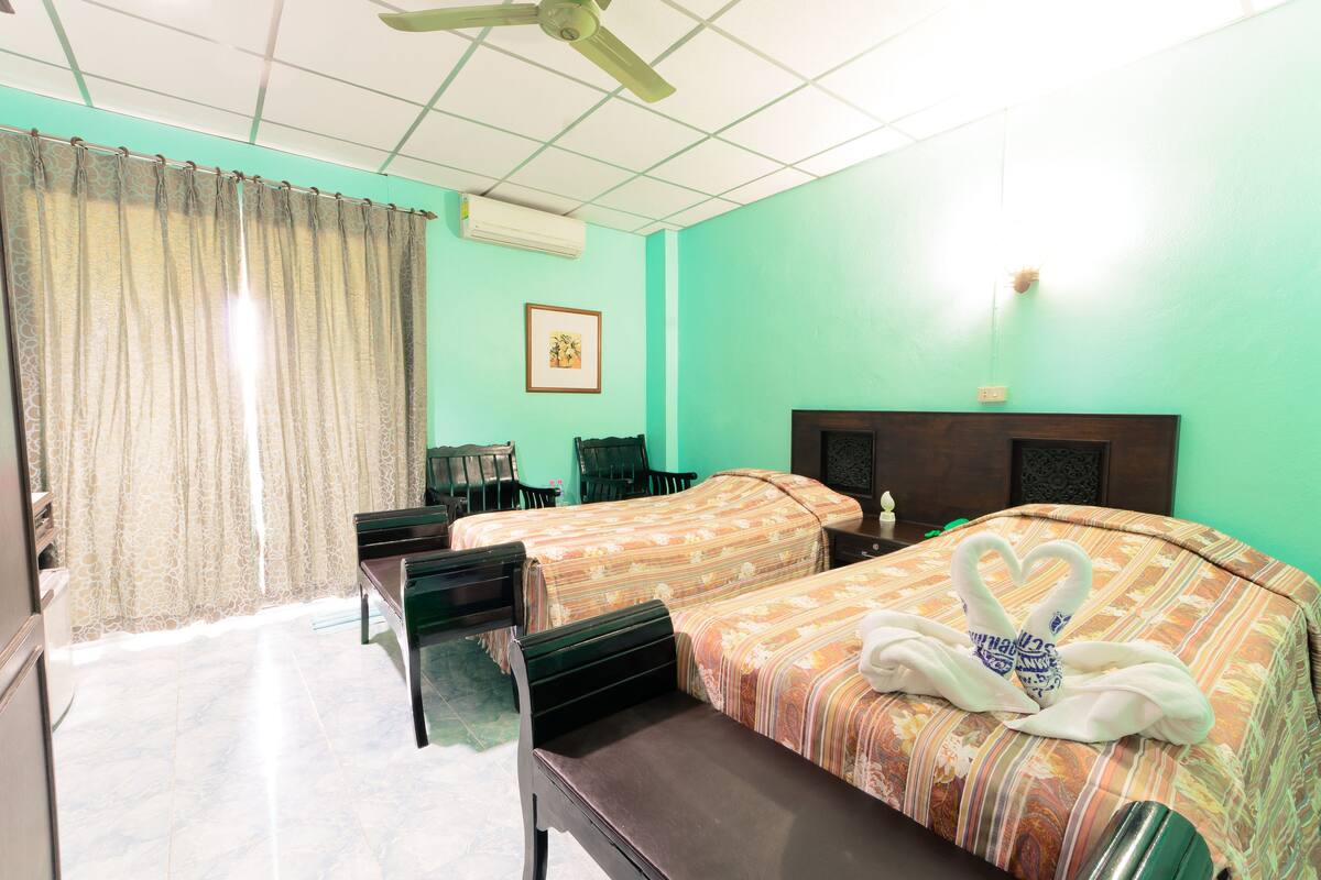 A hotel room with two beds, a desk, a chair, a ceiling fan, and a picture on the wall.