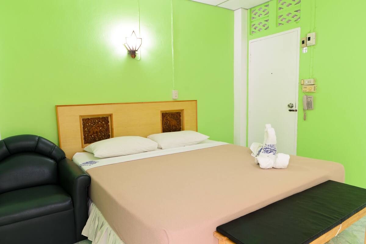A room with a bed, a chair, a bedside table, a wall-mounted phone, and a light fixture.