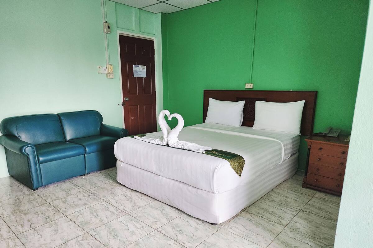 A room with a bed, a blue sofa, a wooden nightstand, and a green wall.