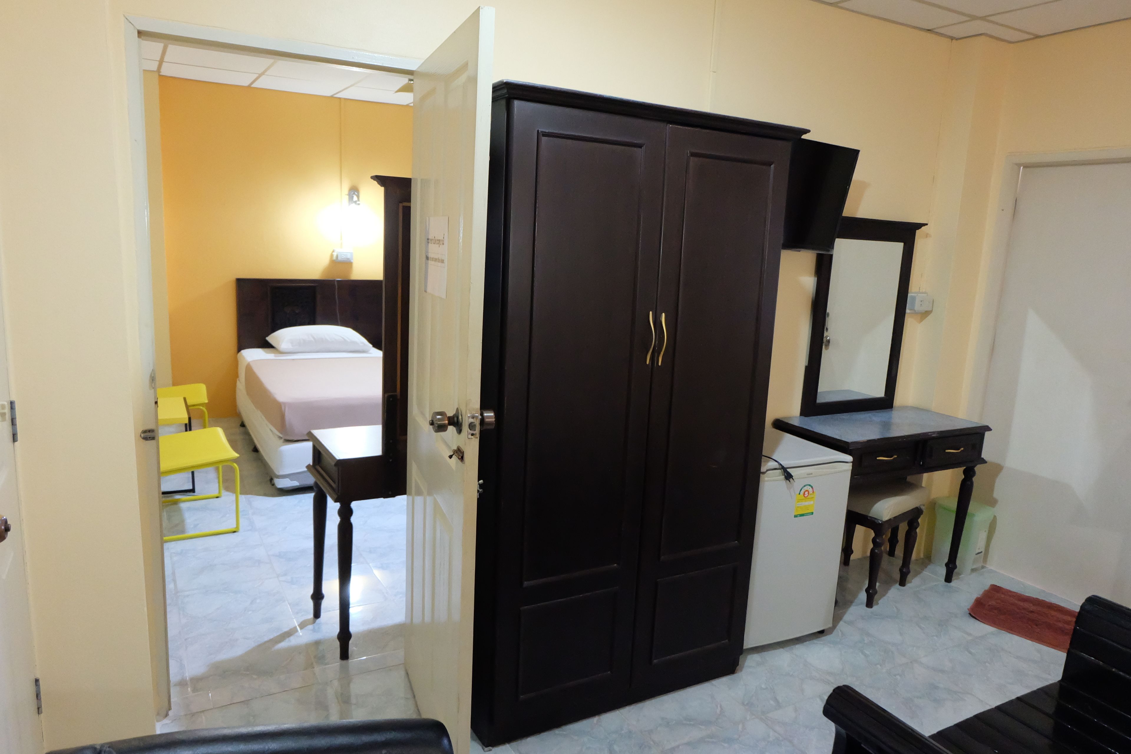 A hotel room with a bed, a wardrobe, a desk, and a small refrigerator.