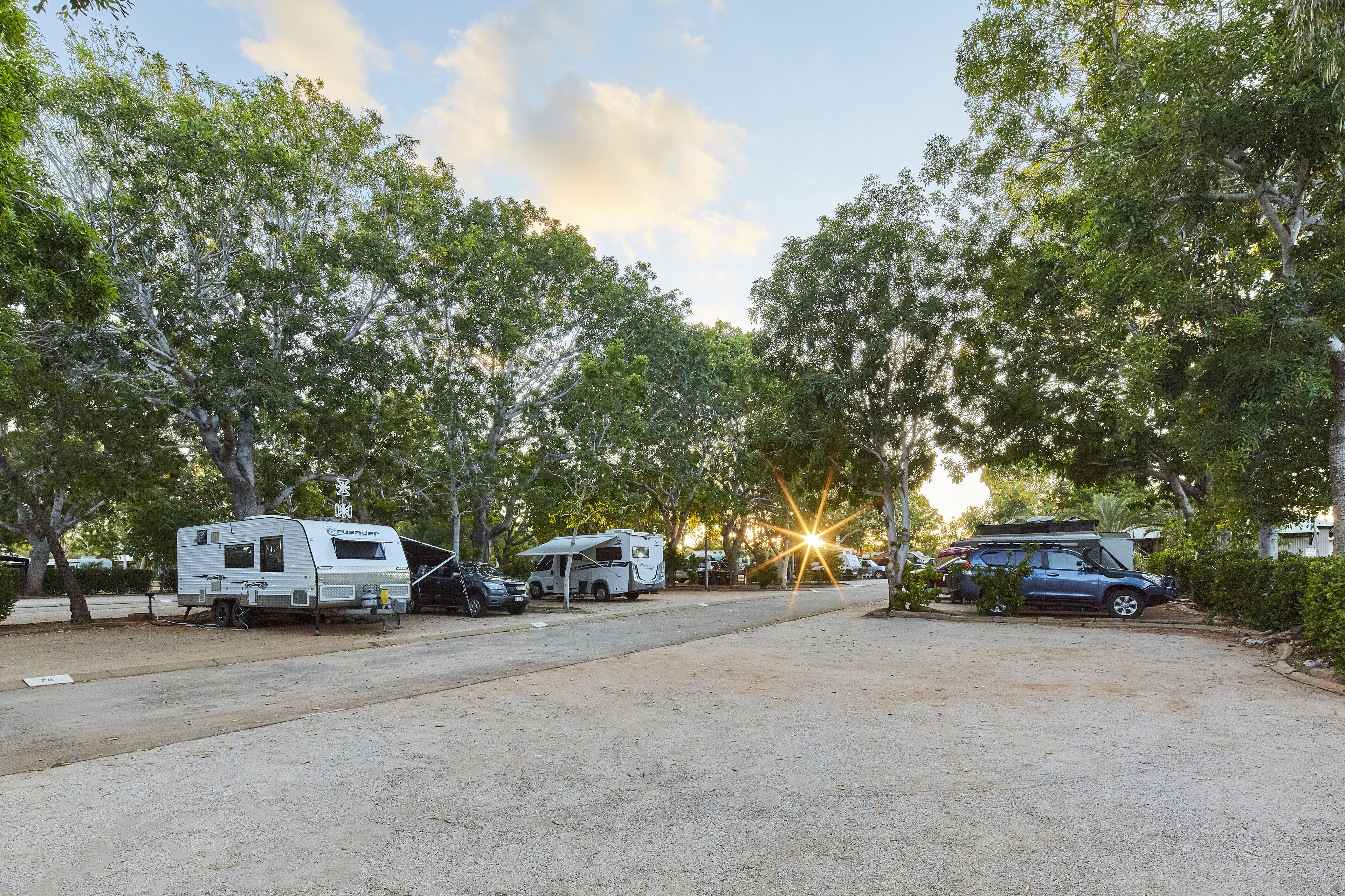 A campground with RVs and cars parked along a gravel road, surrounded by trees.
