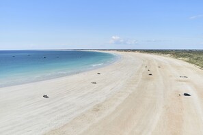 A wide sandy beach with a clear blue sea and a few boats.