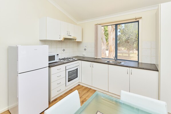 A modern kitchen with white cabinets, a gas stove, an oven, and a window with a view of trees.