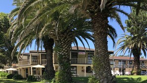 A motel with a two-story structure, outdoor seating, and palm trees. - Half Moon Bay Motel (Auckland)