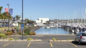 A marina with boats docked, a parking area, and a building with a unique architectural design. - Half Moon Bay Motel (Auckland)