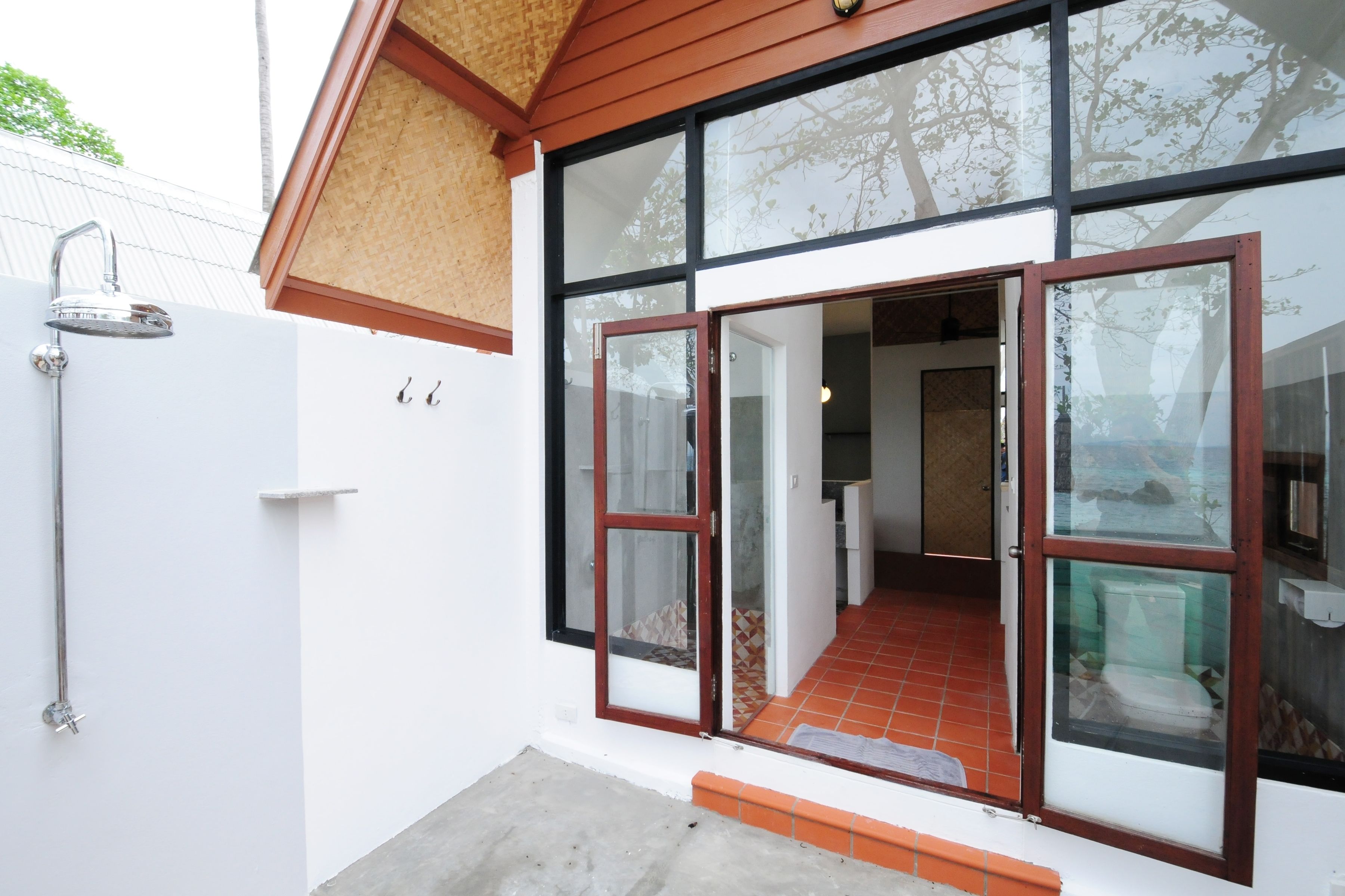 A modern house with a large glass door, a shower, and a tiled patio.