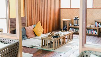 A cozy room with a wooden floor, a sofa with cushions, a coffee table with items, and a bookshelf.