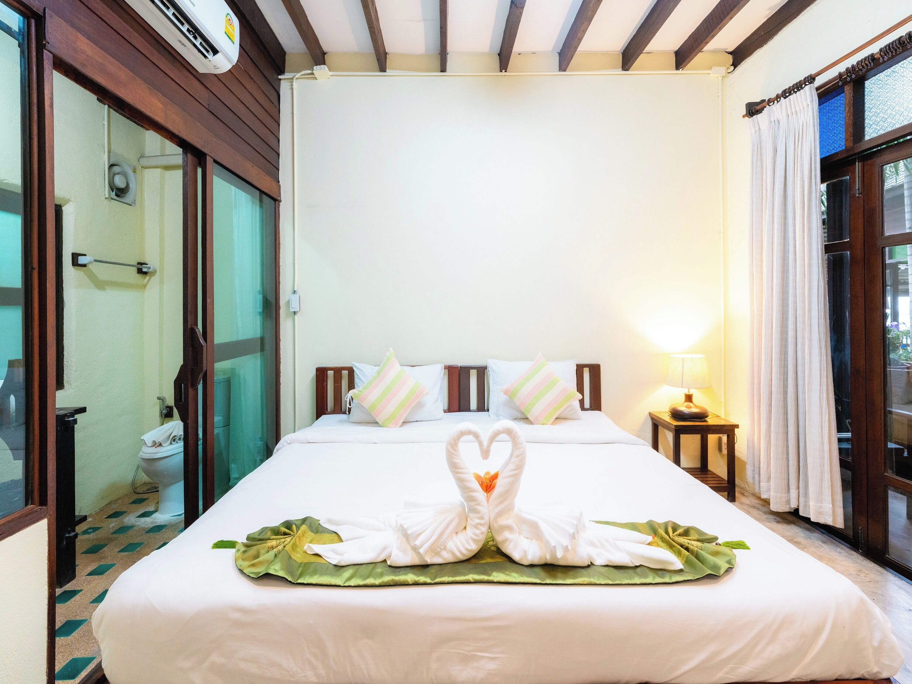 Quarto de hotel com cama, mesa de cabeceira, luminária, janela com cortinas e chuveiro.