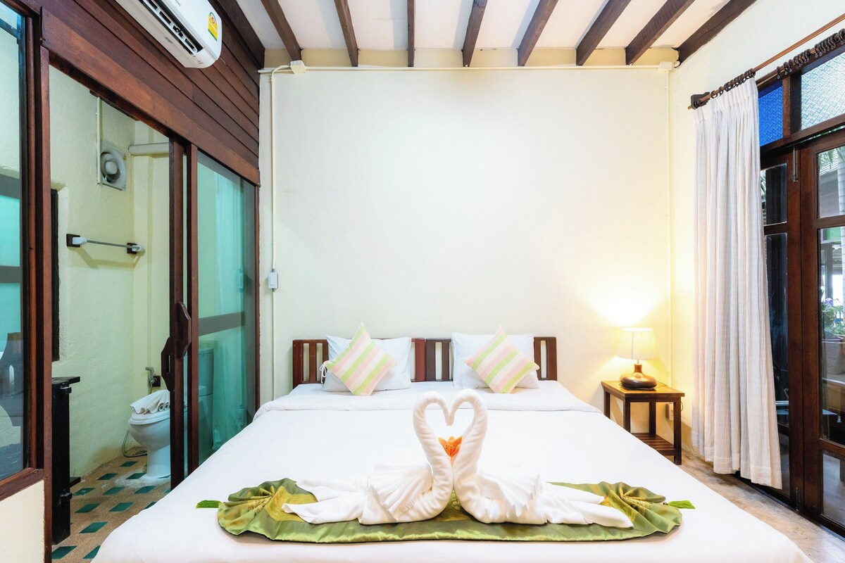 A hotel room with a bed, a nightstand, a lamp, a window with curtains, and a shower area.