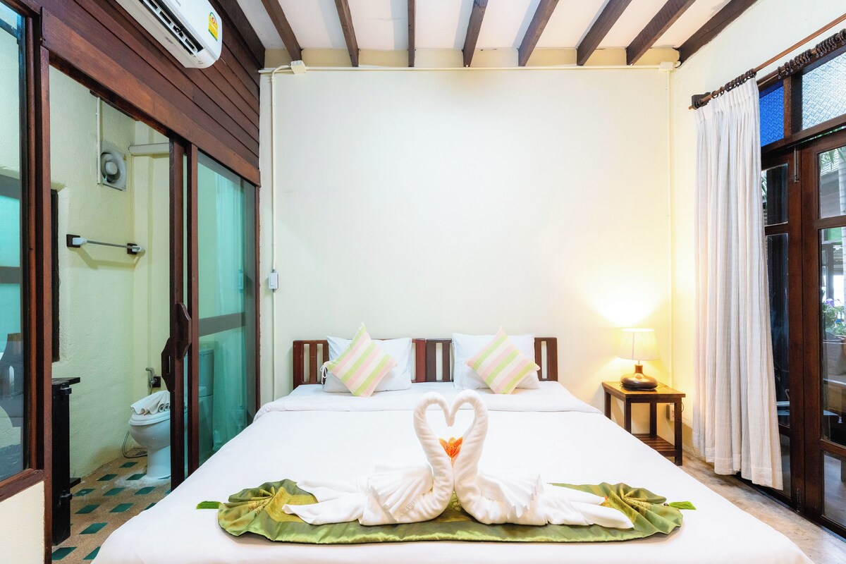 A hotel room with a bed, a nightstand, a lamp, a window with curtains, and a shower area.