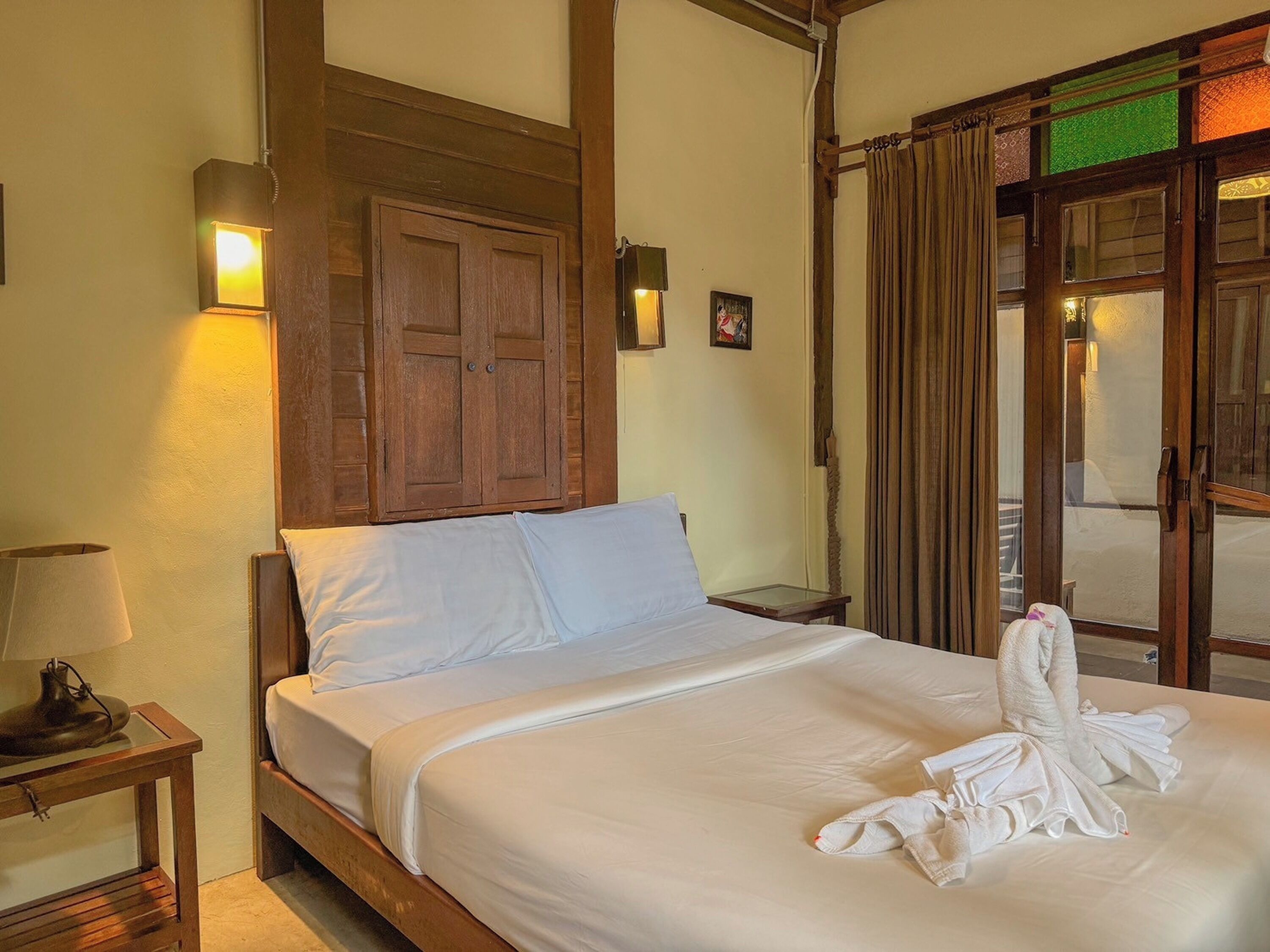 Quarto de hotel com uma cama, guarda-roupa de madeira, mesa de cabeceira com abajur e janela com cortinas.