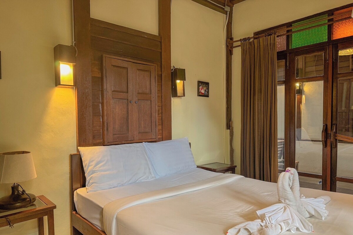 A hotel room with a bed, a wooden wardrobe, a nightstand with a lamp, and a window with curtains.