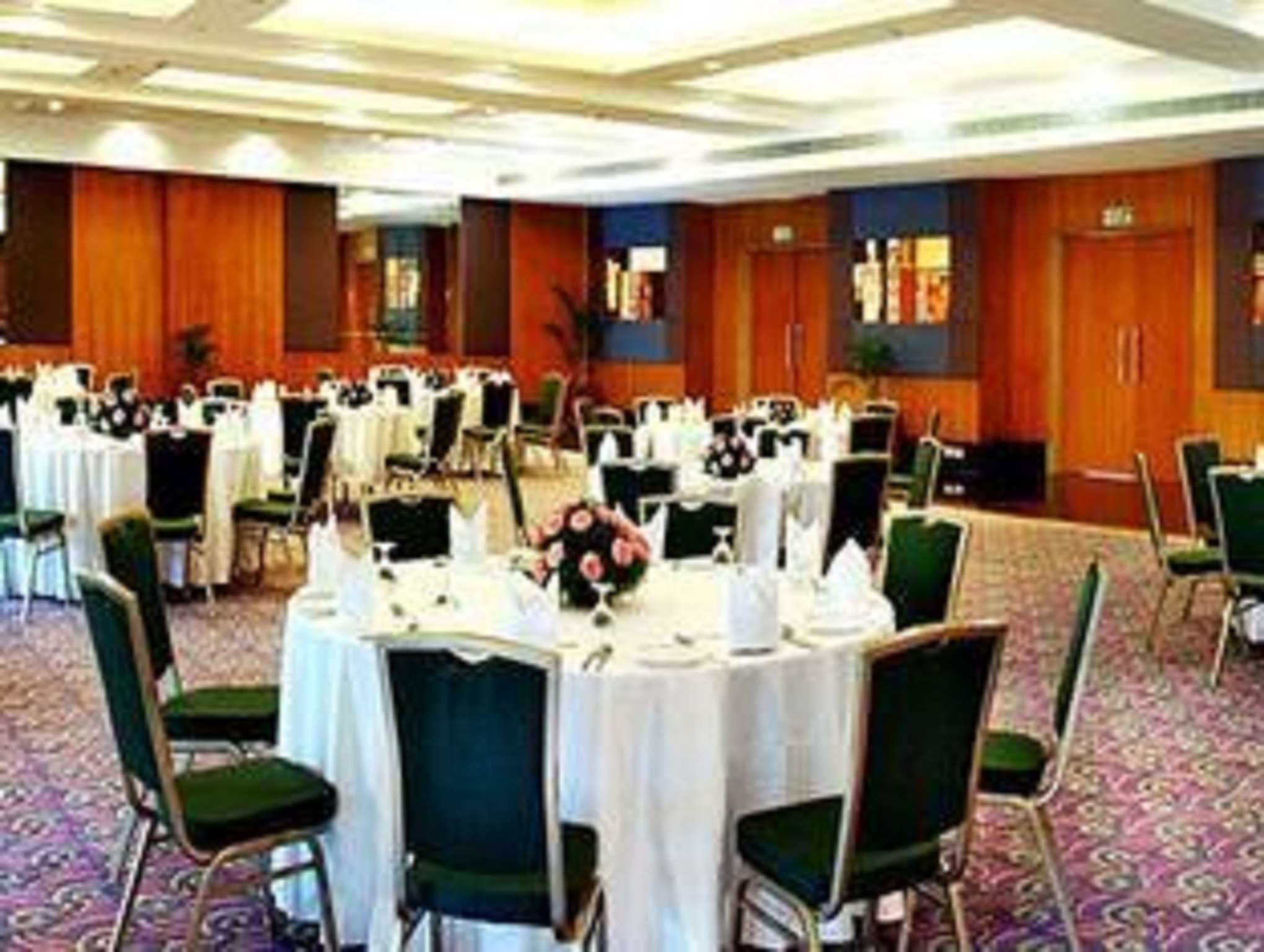 A banquet hall with round tables set for events, green chairs, and a carpeted floor.