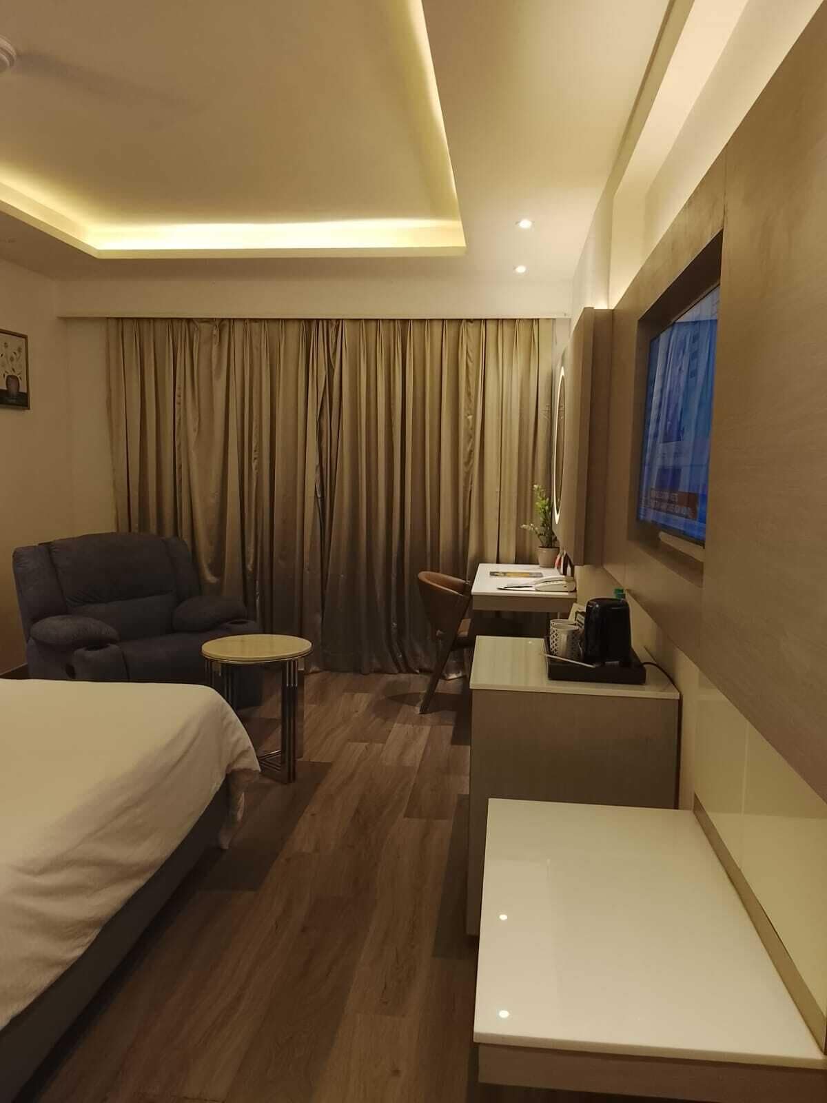 Habitación de hotel con cama, escritorio, silla, una mesita y televisor en la pared.