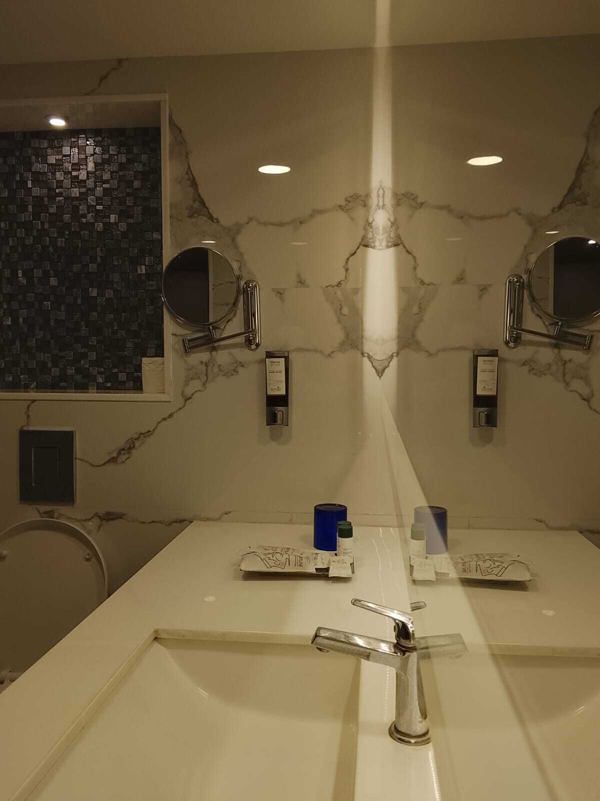 A bathroom with a large mirror, two sinks, and a tiled wall.