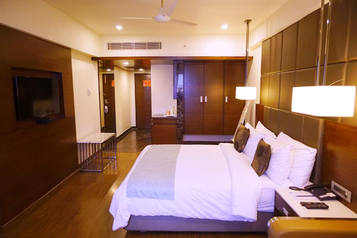 Habitación de hotel con una cama grande, lámparas de noche, un televisor y un escritorio con teléfono y controles remotos.