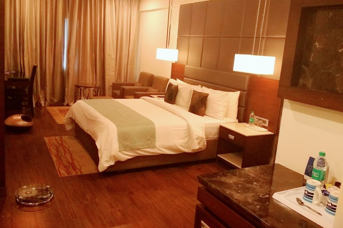 Habitación de hotel con cama, mesitas de noche, escritorio, silla, sofá, alfombra, cortinas y ventilador de techo.