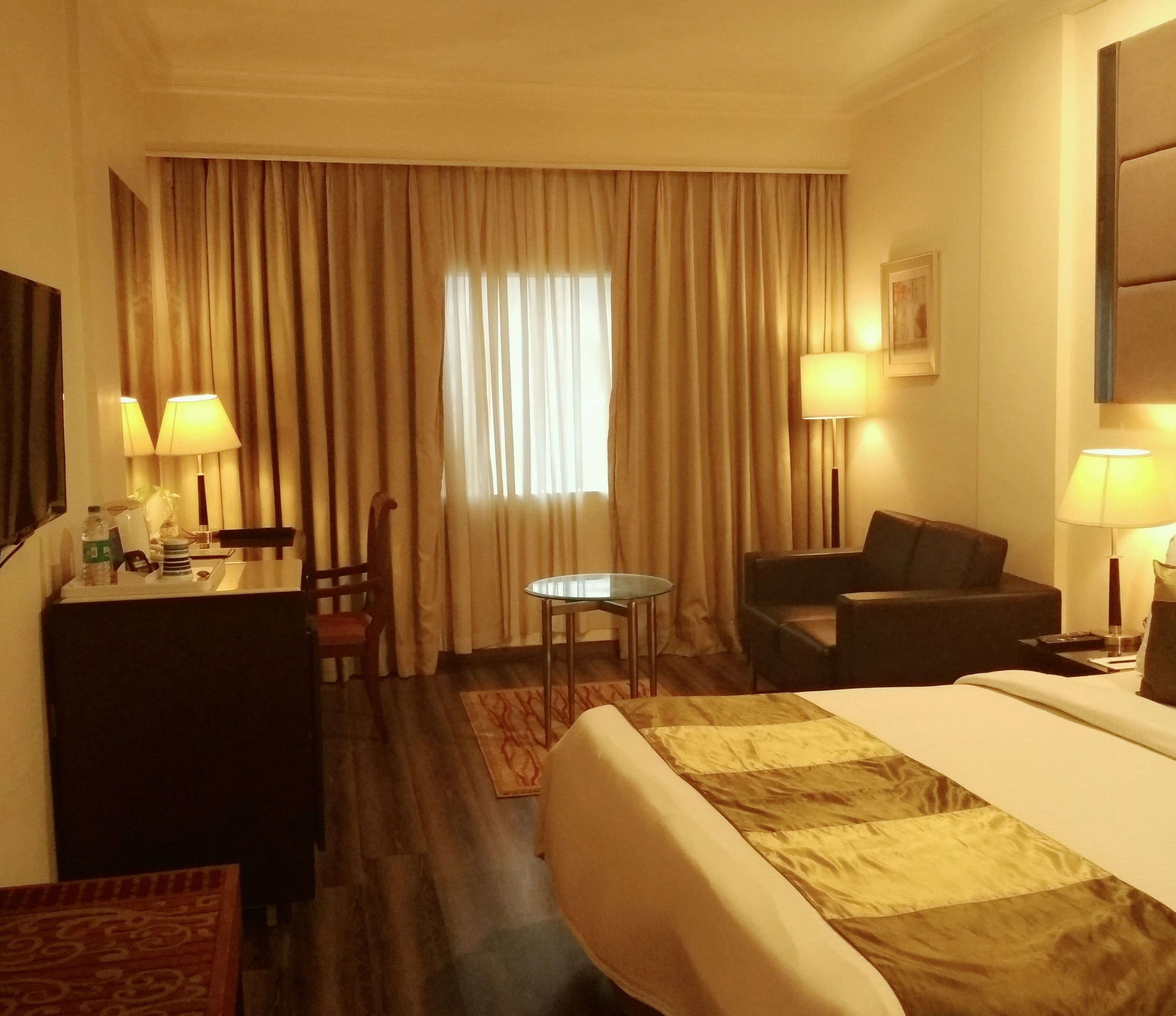 Une chambre d’hôtel comprenant un lit, un bureau, une chaise, une petite table et deux lampes.