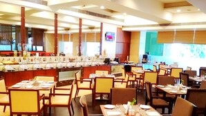 A restaurant with multiple dining tables and chairs, a counter with a display of food items, and a television screen mounted on the wall. - Fortune Murali Park, Vijayawada - Member ITC Hotels' Group (Vijayawada)