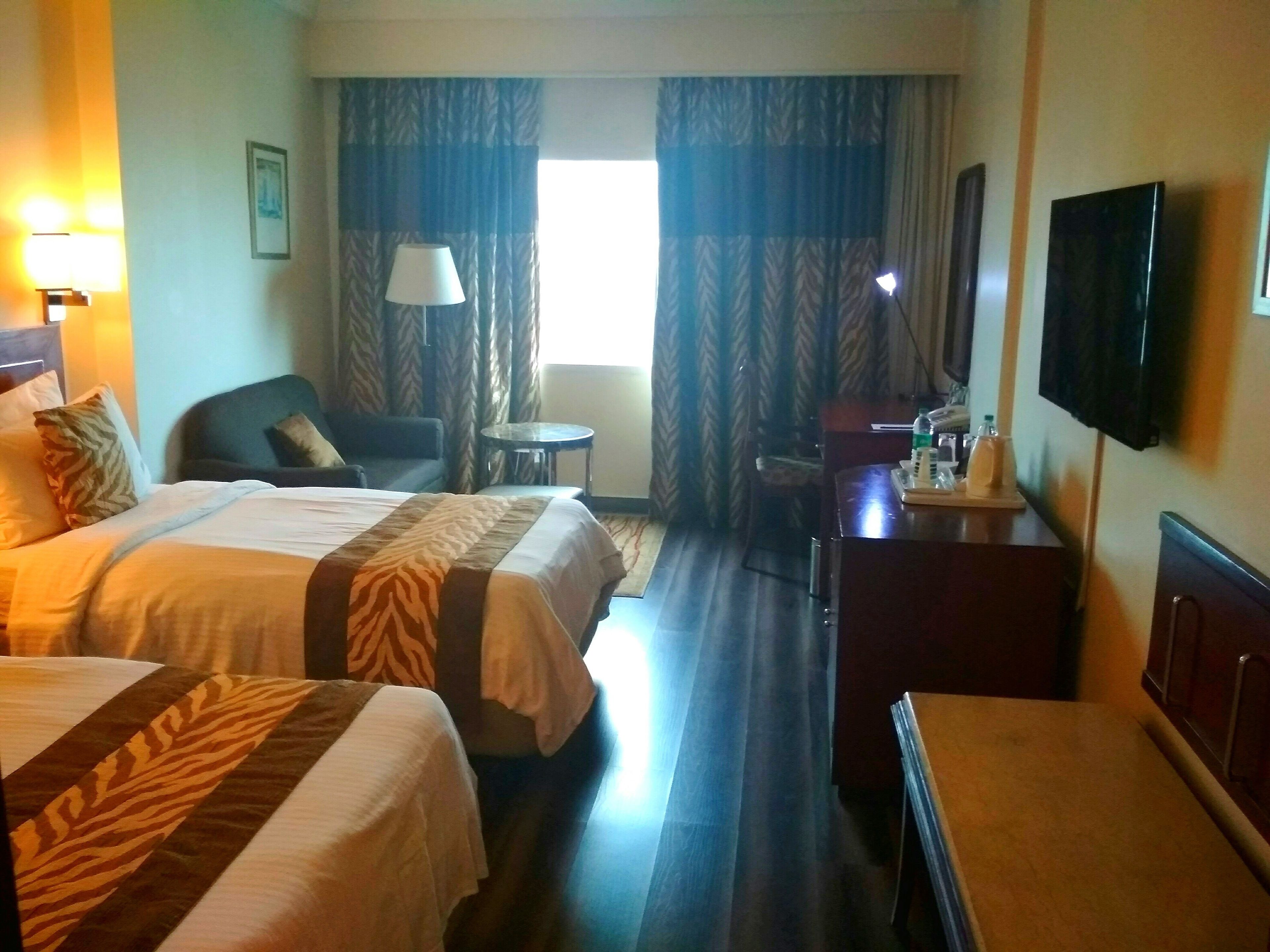 Habitación de hotel con dos camas, un escritorio, una silla, un televisor y una ventana con cortinas.