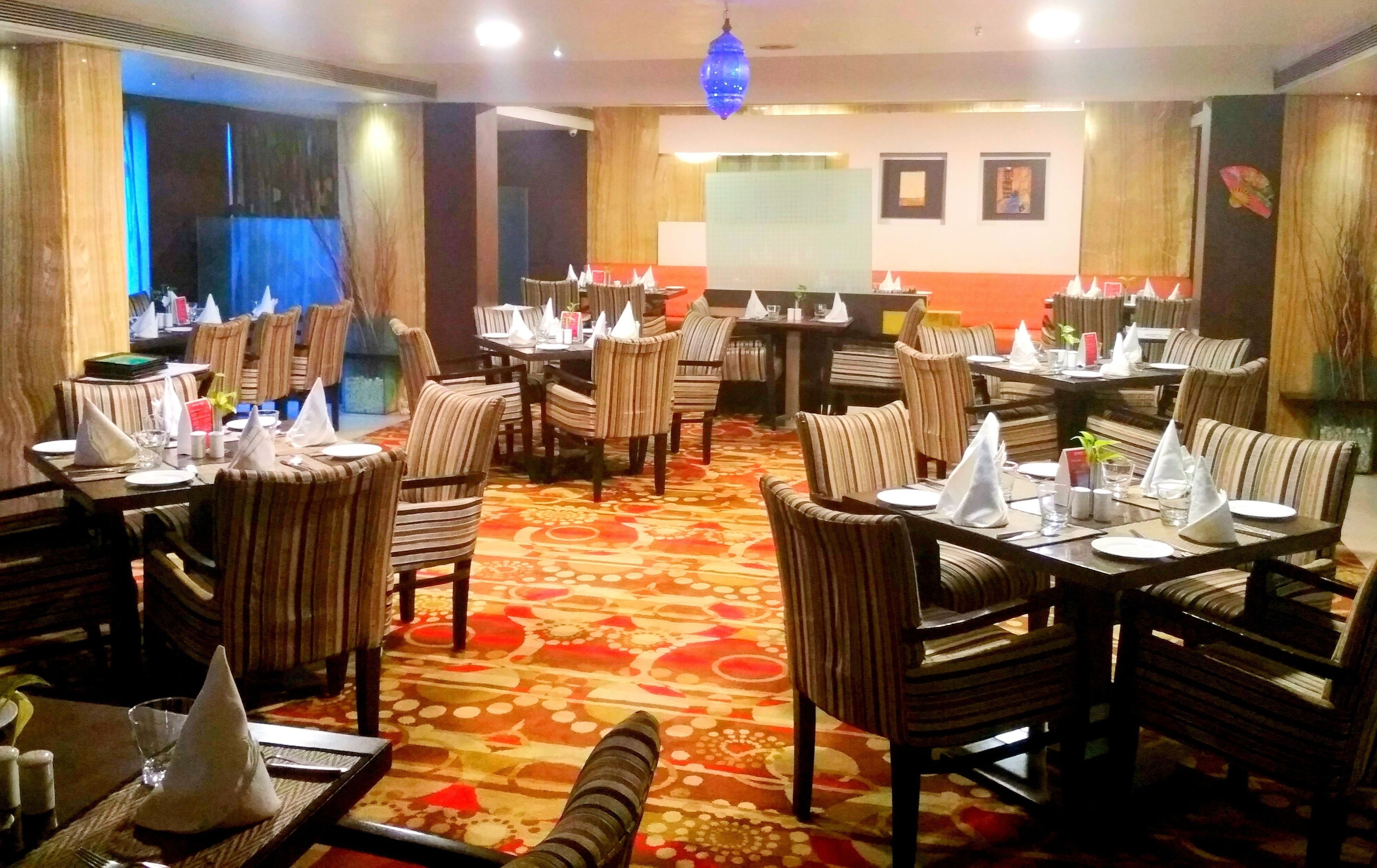 Ein Restaurant mit gestreiften Stühlen und Tischen, einem gemusterten Teppich und einer blauen Hängelampe.