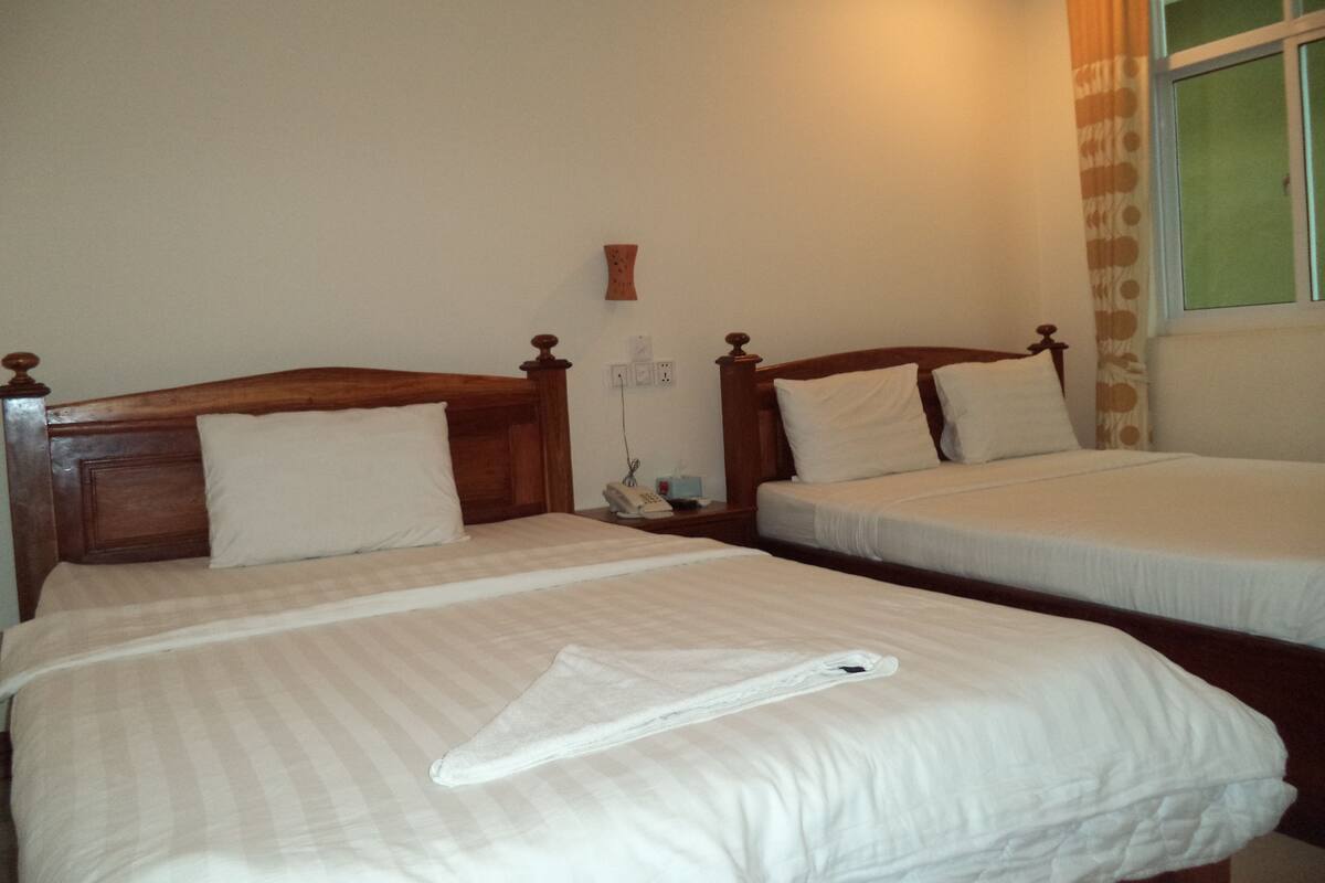 Ein Hotelzimmer mit zwei Einzelbetten, einem Nachttisch mit Telefon, einer Wandvase und einem Fenster mit Vorhängen.