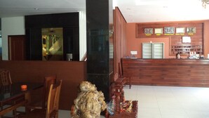 Un vestíbulo de hotel con mostrador de recepción, sillas de madera, una mesa de comedor y una escultura decorativa.