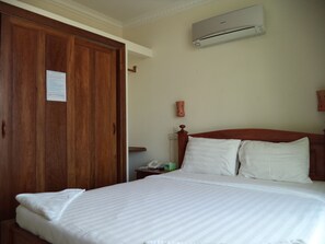 A hotel room with a wooden wardrobe, a bed with white bedding, a nightstand, a telephone, and an air conditioning unit on the wall. - Go In Hotel (Phnom Penh)