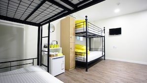A compact room with bunk beds, a small kitchenette, and a TV mounted on the wall.
