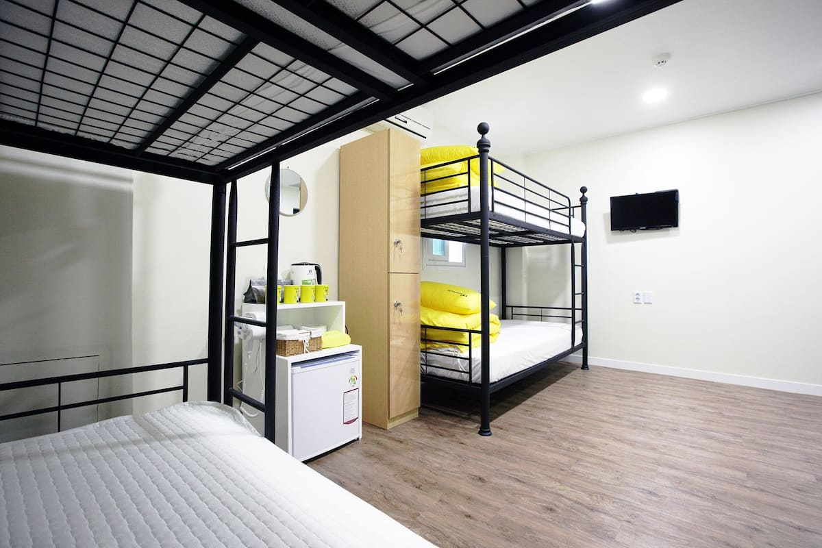 A compact room with bunk beds, a small kitchenette, and a TV mounted on the wall.