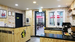 A reception area with a wooden counter, a welcome sign, and a view of an outdoor patio with picnic tables and umbrellas.