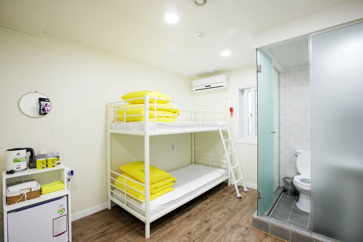 A bunk bed with yellow pillows, a white shelf with toiletries, a white cabinet, and a shower area.