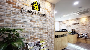 A guesthouse reception area with a brick wall, a reception desk labeled "INFORMATION," and a display of daily tour brochures.