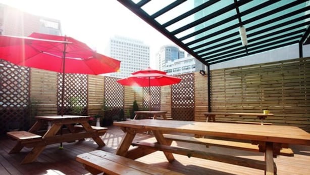 An outdoor patio with wooden picnic tables and red umbrellas.