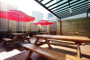 An outdoor patio with wooden picnic tables and red umbrellas. - 24 Guesthouse Myeongdong Avenue (Seoul)